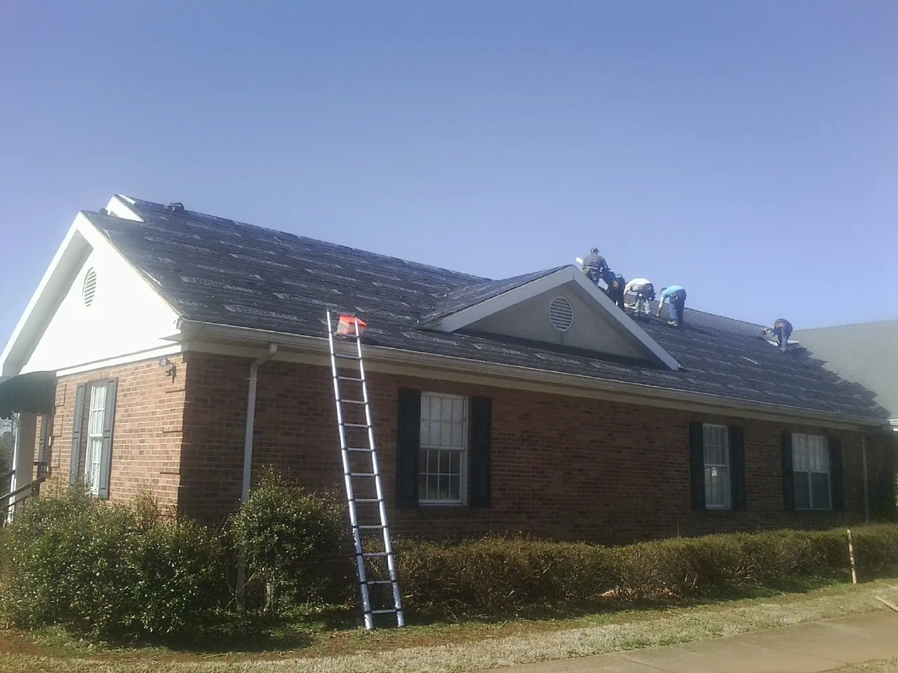 Crew tearing shingles off a brick ranch roof with a ladder set — Metal Roof Repair work by our crew in Forest
