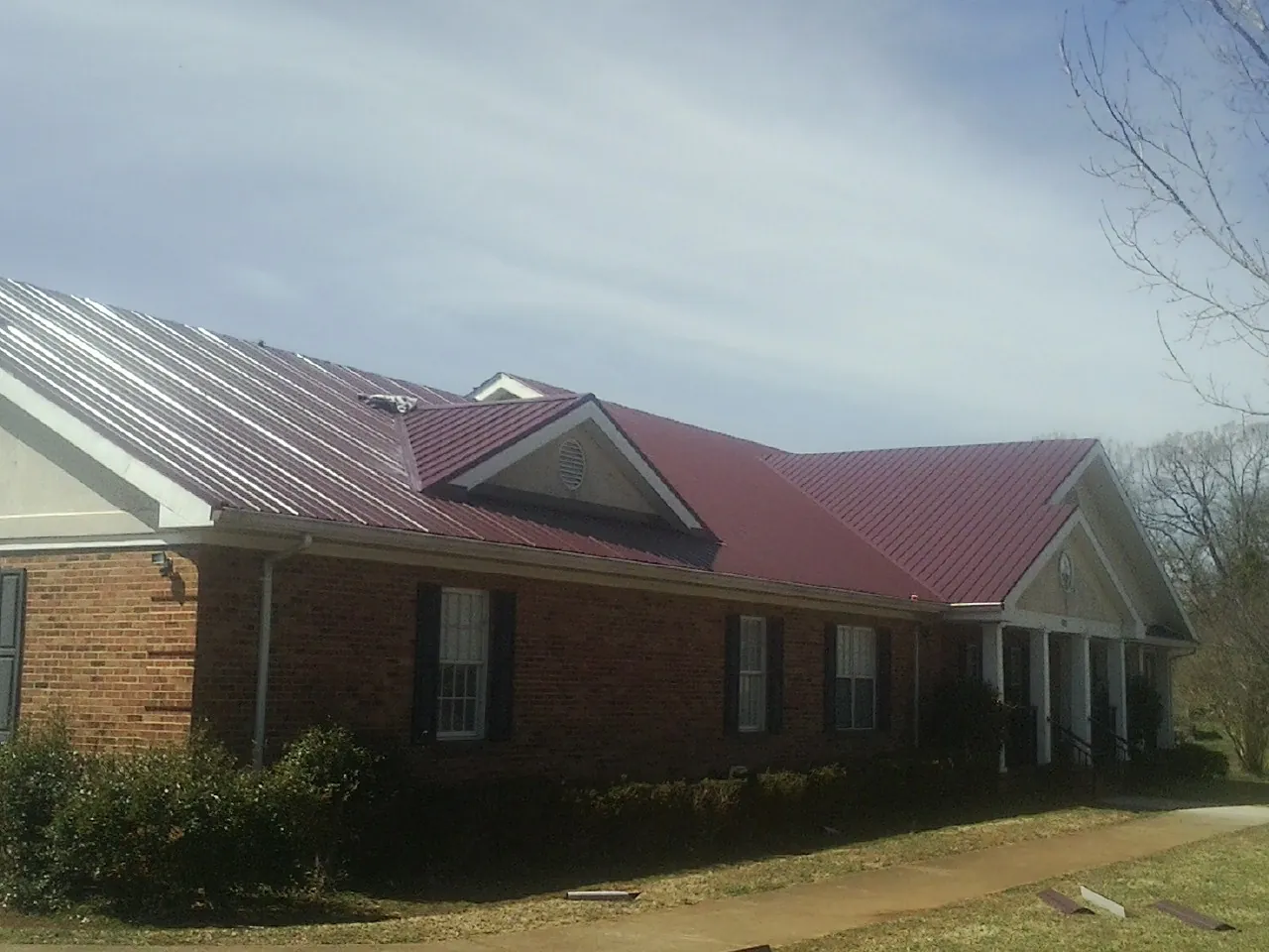 Red metal roof with gabled entries on a long brick building, from a Hail Damage Roof Repair job in Forest