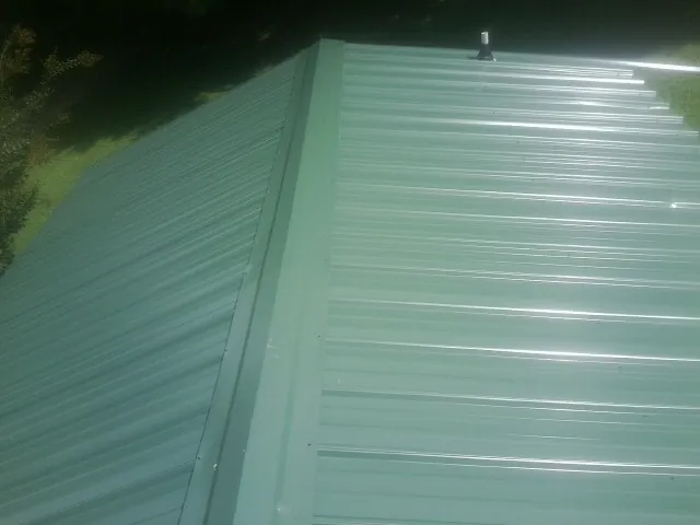 New green metal panels meeting at the ridge of a roof — Flat Roof Repair work by our crew in Forest