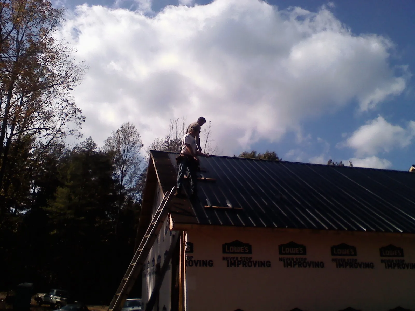Roofer fastening dark metal panels high against a cloudy sky, from a Roof Inspection job in Forest